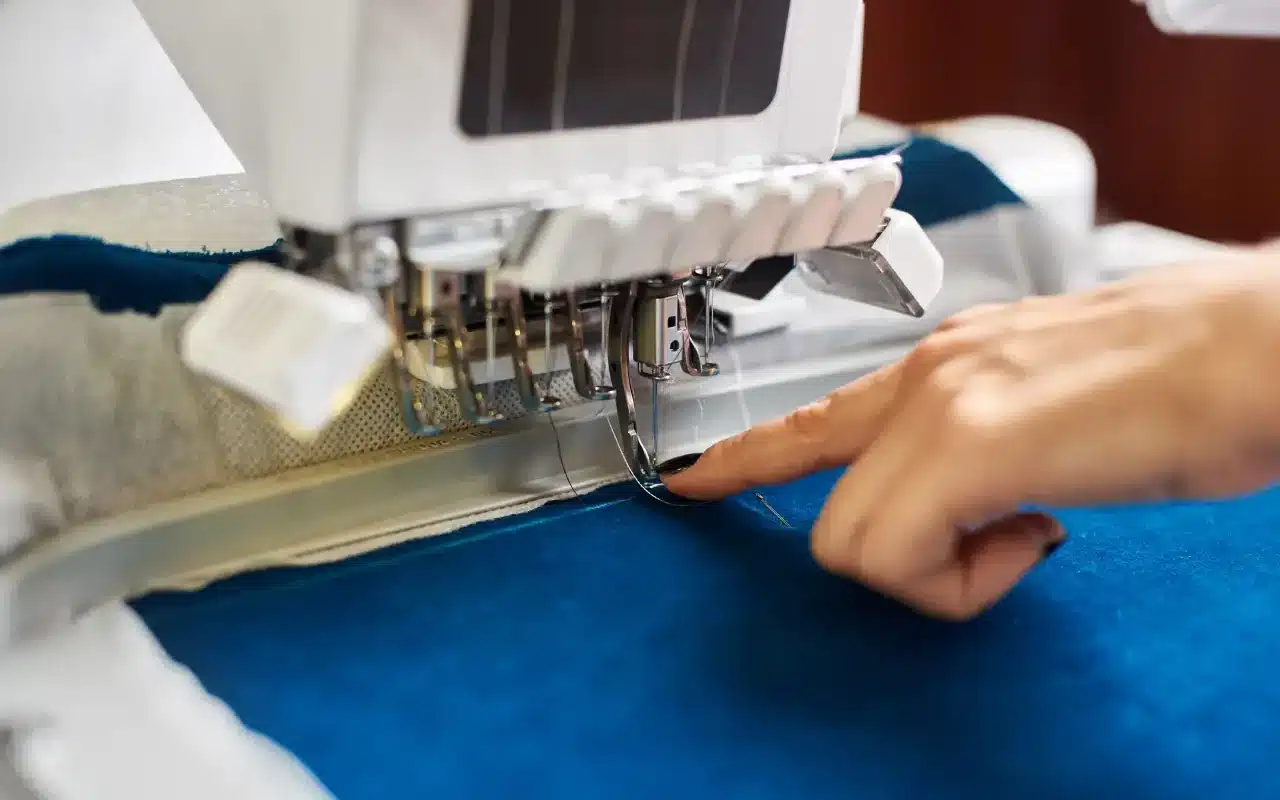 Gros plan de la main de la femme à la machine à broder informatisée sur fond de détail textile bleu.